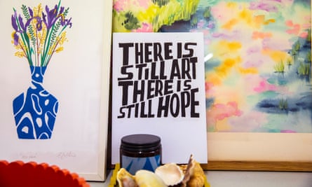 تابلویی از گل‌ها در گلدانی با گردن باریک در کنار هنر که روی آن نوشته شده است: «هنوز هنر وجود دارد.  هنوز امید هست» در مقابل یک نقاشی انتزاعی